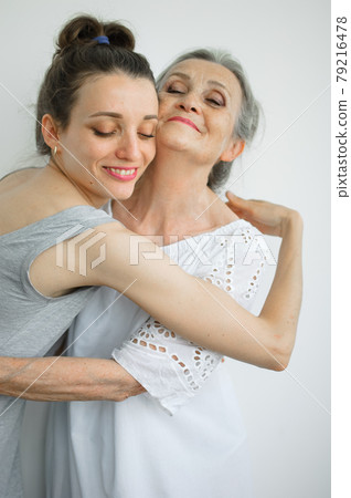 Happy senior mother is hugging her adult daughter, the women are laughing together, sincere family of different age generations having fun on white background Happy senior mother is hugging her adult daughter, the women are laughing together, sincere family of different age generations having fun on white background 79216478