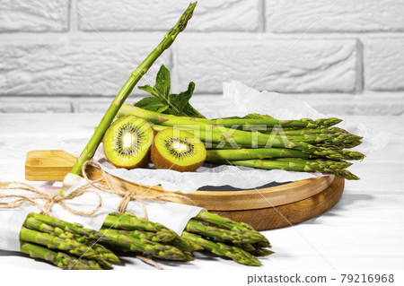 Fresh Green Fruit and Vegetable: kiwi, mint and asparagus on wooden board on white Background. Healthy ingridient for Smoothie. Bunch of Asparagus. 79216968