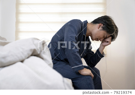 A man in his 50s sitting in bed and holding his head 79219374