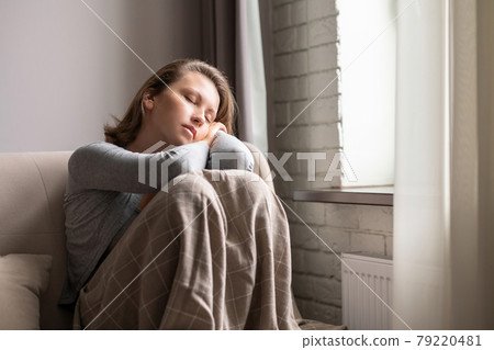 Portrait of young beautiful tired woman sleeping sitting on the couch covering plaid near window Portrait of young beautiful tired woman sleeping sitting on the couch covering plaid near window 79220481