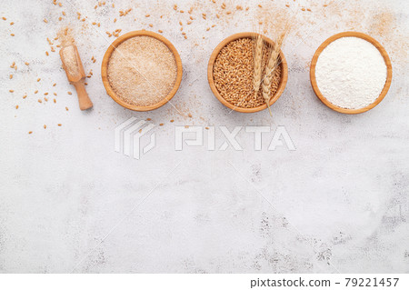 Wheat grains , brown wheat flour and white wheat flour in wooden bowl set up on white concrete background. 79221457