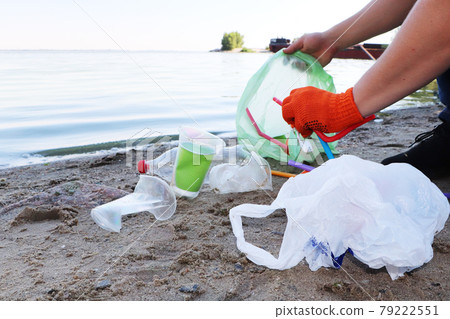 Garbage collection on the beach. Plastic and packages scattered on the beach. A man collects plastic. Ecology protection concept Garbage collection on the beach. Plastic and packages scattered on the beach. A man collects plastic. Ecology protection concept 79222551