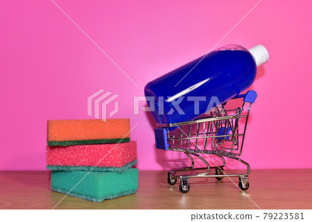 Washing sponges and detergent bottle in a shopping cart on a pink background. Washing sponges and detergent bottle in a shopping cart on a pink background. 79223581