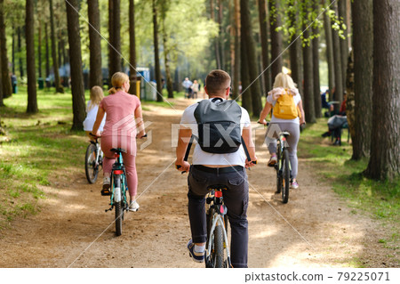 A group of cyclists with backpacks ride bicycles on a forest road enjoying nature A group of cyclists with backpacks ride bicycles on a forest road enjoying nature 79225071