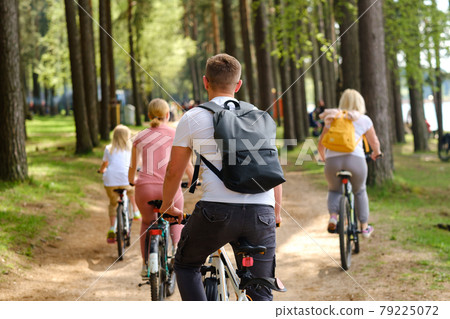 A group of cyclists with backpacks ride bicycles on a forest road enjoying nature A group of cyclists with backpacks ride bicycles on a forest road enjoying nature 79225072