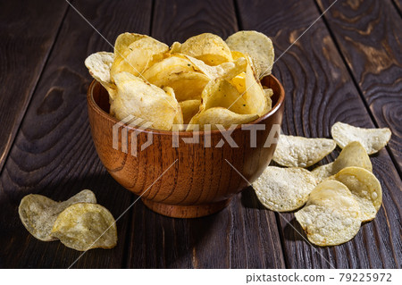 Crispy organic potato chips with dill in a brown wooden bowl on a black wooden table. Crispy organic potato chips with dill in a brown wooden bowl on a black wooden table. 79225972