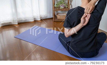 A man doing yoga in the room. An image of a man trying to pose a cow's face. 79230173
