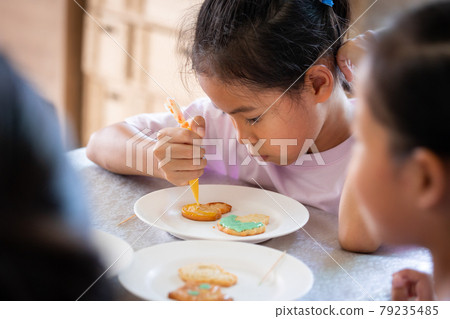 Close up asian child girl squeezing icing cream to decorate cookies with friend with fun. DIY homemade kid art and craft concept. Close up asian child girl squeezing icing cream to decorate cookies with friend with fun. DIY homemade kid art and craft concept. 79235485