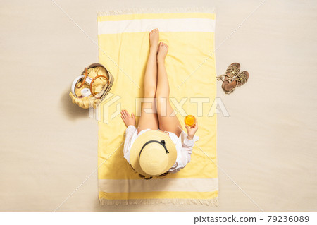 Alone woman in straw hat and bikini sitting on yellow beach towel with bag, headphones, juice. Female relaxation on the sand beach at summer vacation. Top, aerial view Alone woman in straw hat and bikini sitting on yellow beach towel with bag, headphones, juice. Female relaxation on the sand beach at summer vacation. Top, aerial view 79236089