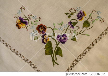 Embroidered corner with brown and purple pansies, blue flowers on curved branches and green leaves 79236134