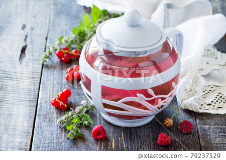 Hot fruit berry tea with mint, red currant and red raspberries on a wooden kitchen table. Hot fruit berry tea with mint, red currant and red raspberries on a wooden kitchen table. 79237529