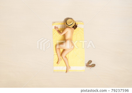 Alone naked woman in straw hat lying and sleeping on yellow beach towel. Female relaxation on the sand of the beach at summer vacation. Top, aerial view 79237596