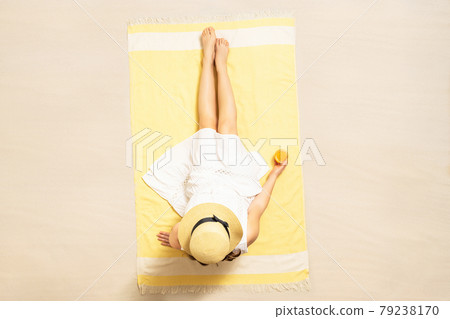 Alone woman in straw hat and dress sitting on yellow beach towel and drinking orange juice. summer. Top, aerial view Alone woman in straw hat and dress sitting on yellow beach towel and drinking orange juice. summer. Top, aerial view 79238170