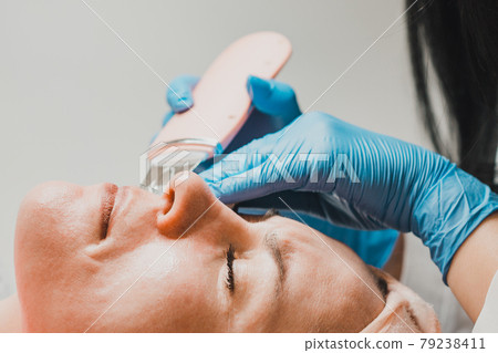 The beautician cleanses the patient's skin with an ultrasonic scrubber, moisturizing, cleansing and skin care. The beautician cleanses the patient's skin with an ultrasonic scrubber, moisturizing, cleansing and skin care. 79238411