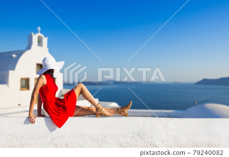 Santorini travel tourist brunette woman in red dress visiting famous white Oia village. 79240082