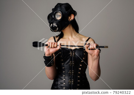 Sensual woman in black leather corset with gas mask and riding crop in hand 79240322