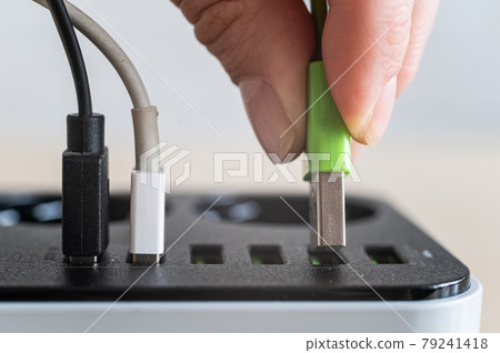 Modern convenient multi-port usb charger for devices. Close-up of a female hand plugging multi-colored cables into a power outlet. Macro. Modern convenient multi-port usb charger for devices. Close-up of a female hand plugging multi-colored cables into a power outlet. Macro. 79241418