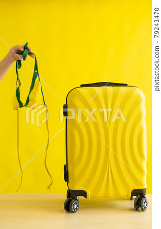 Faceless woman going on a trip holding a bikini next to a suitcase on a yellow background. A female hand is preparing a swimsuit for summer vacation. Copy space. Faceless woman going on a trip holding a bikini next to a suitcase on a yellow background. A female hand is preparing a swimsuit for summer vacation. Copy space. 79241470