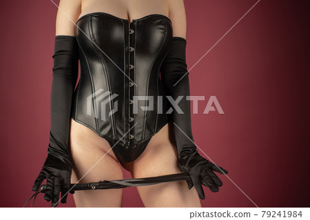 Beautiful young woman in a leather corset posing with a whip in her hands Beautiful young woman in a leather corset posing with a whip in her hands 79241984