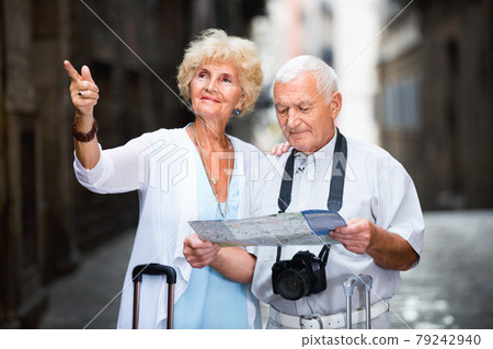 Senior couple of tourists with map and city guide walking Senior couple of tourists with map and city guide walking 79242940