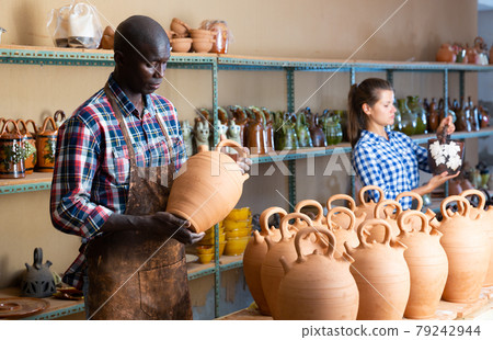 Woman and man artisans in apron having ceramics in store warehouse 79242944