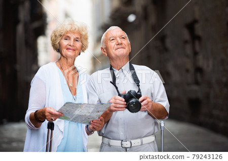 Senior man photographing sights while his wife looking map near old cathedral Senior man photographing sights while his wife looking map near old cathedral 79243126