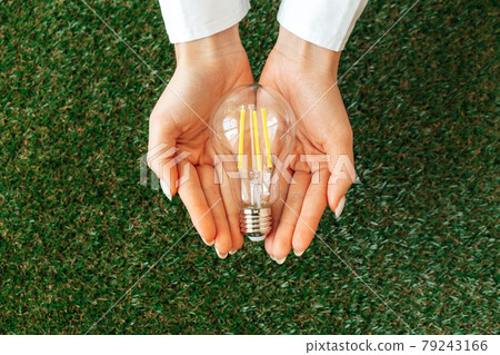 Woman holding lamp in hands above the grass 79243166