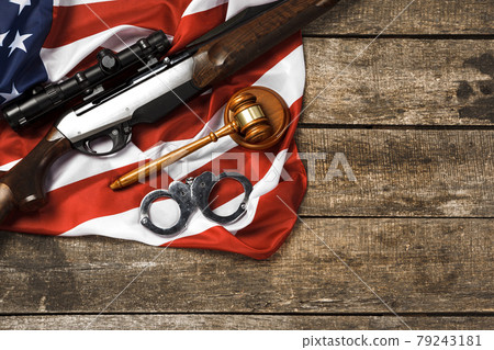 Wooden judge gavel and hunting rifle over USA flag on wooden background Wooden judge gavel and hunting rifle over USA flag on wooden background 79243181