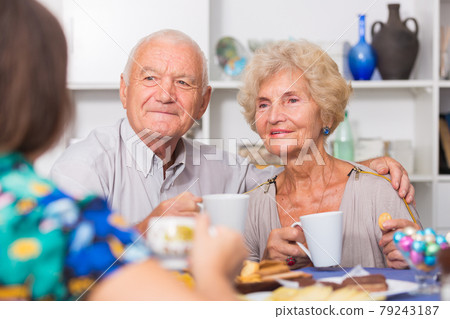 Happy mature couple drinking tea with female guest Happy mature couple drinking tea with female guest 79243187