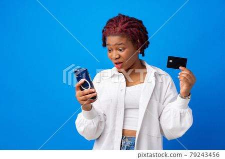 African american woman holding smartphone and credit card against blue background 79243456