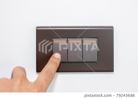 Close up fingers is turning on or turning off the brown light-switch on stenciled white wall. Close up fingers is turning on or turning off the brown light-switch on stenciled white wall. 79243686