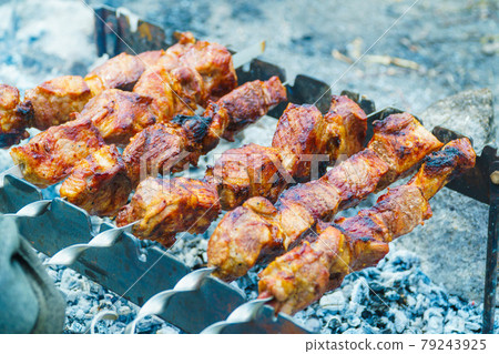 Appetizing raw meat kebab is cooked on the grill on the wood, in the open air. The kebab is cooked on skewers. 79243925