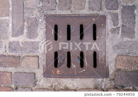Drain hatch in the form of a grate on the road laid out with tiles. Drain hatch in the form of a grate on the road laid out with tiles. 79244950