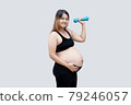 Sporty pregnant woman exercising with dumbbells on gray background. Cheerful pregnant woman exercising at home. 79246057