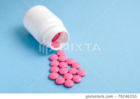Pink pills fall out of a white container on a blue background. Pink pills fall out of a white container on a blue background. 79246350