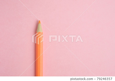 Orange pencil on pink paper background. Close up. 79246357