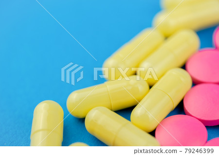 Pink pills and yellow medicine on a blue background. Cocept treatment selection. Close up. 79246399