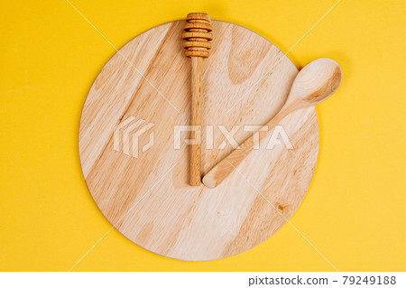 Clock is in on a wooden surface. Lunch time concept. On a yellow background Clock is in on a wooden surface. Lunch time concept. On a yellow background 79249188