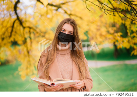 Portrait of a beautiful adult young woman on the background of autumn in park in medical face mask 79249531