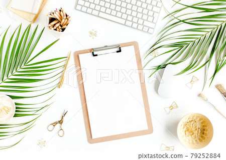 Flat lay home office desk. Female workspace with computer, clipboard, tropical palm leaves, accessories on white background. Top view.  79252884