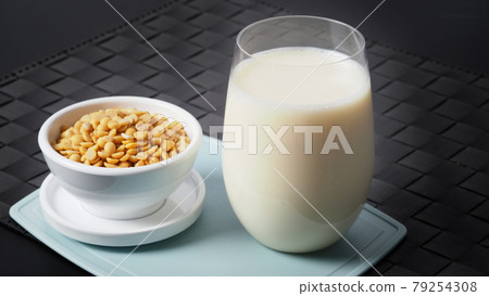 Soy milk with no sugar added in a glass on a green color plastic plate mat. Close-up images of home made healthy soy milk drink and soy beans in small bowl. Black background in a studio shot. Soymilk. Soy milk with no sugar added in a glass on a green color plastic plate mat. Close-up images of home made healthy soy milk drink and soy beans in small bowl. Black background in a studio shot. Soymilk. 79254308
