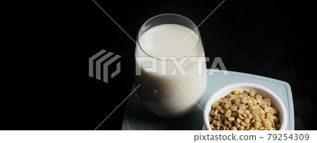 Soy milk with no sugar added in a glass on a green color plastic plate mat. Close-up images of home made healthy soy milk drink and soy beans in small bowl. Black background in a studio shot. Soymilk. 79254309