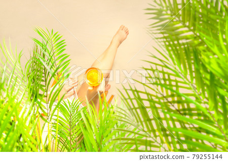 Alone woman sitting under palm tree branches with glass of water with piece orange. Female relaxation on the sand of the beach at summer vacation. Top view Alone woman sitting under palm tree branches with glass of water with piece orange. Female relaxation on the sand of the beach at summer vacation. Top view 79255144