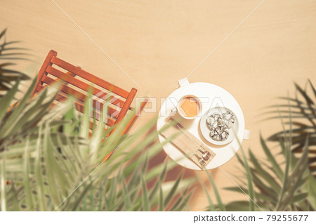 Cup of coffee with chocolate cookies on the table with wooden chair under palm trees on the sandy beach. Outdoors cafe. Top view 79255677