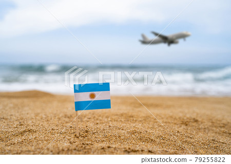 Flag of Argentina in the form of a toothpick in the sand of beach opposite sea wave with landing airplane. Travel concept Flag of Argentina in the form of a toothpick in the sand of beach opposite sea wave with landing airplane. Travel concept 79255822