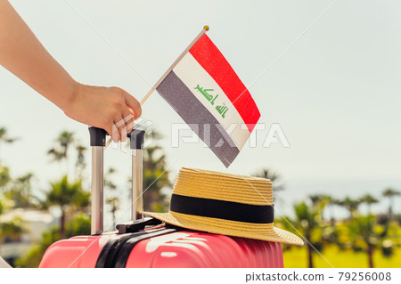 Woman with pink suitcase, hat and Iraq flag standing on passengers ladder and getting out of airplane opposite sea coastline with palm trees. Woman with pink suitcase, hat and Iraq flag standing on passengers ladder and getting out of airplane opposite sea coastline with palm trees. 79256008