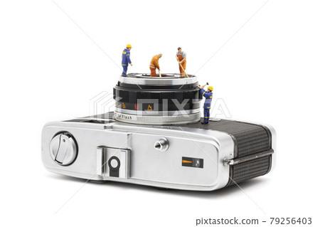 Miniature people cleaning old camera lenses on white background. Miniature people cleaning old camera lenses on white background. 79256403