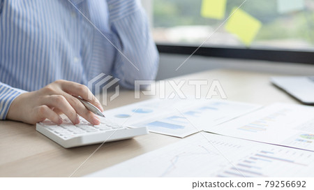 Young Asian businesswoman presses a calculator to calculate income tax and corporate income in a private office, Finance, Accounting, Tex, Statistical graphs of marketers investing in real estate. 79256692