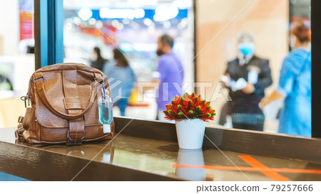 Mini portable alcohol gel bottle to kill Corona Virus(Covid-19) hang on a brown leather shoulder bag on counter in coffee shop.New normal lifestyle. Health care concept. Selective focus on alcohol gel 79257666
