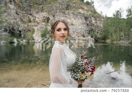 close up. The bride in a white dress with a red bouquet on the bank of a river . close up. The bride in a white dress with a red bouquet on the bank of a river . 79257888